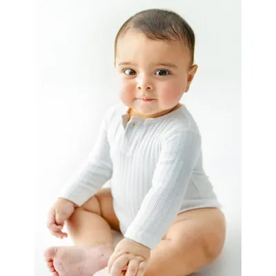 The sweetest six month smile. This portrait captures the adorable chubby cheeks and bright eyes of a baby at their half birthday milestone, sitting proudly in a simple white onesie.