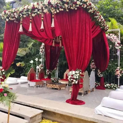 This outdoor mandap is a vision in red. We used luxurious velvet drapes, floral tassels, and a crystal chandelier to create a royal setting against a lush green backdrop, perfect for a classic Indian wedding ceremony.
