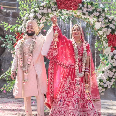 A triumphant and joyous moment as the bride and groom raise their hands after the Varmala ceremony, standing before a magnificent waterfall and floral arch.