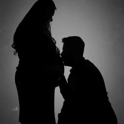 A beautiful and intimate silhouette portrait of a couple. The dad-to-be kissing the baby bump is a classic, tender moment that looks stunning in black and white.