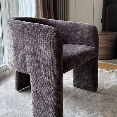 A modern accent chair upholstered in a rich, textured grey fabric. The chair's unique, sculptural form with its solid block legs makes it a statement piece in any room.