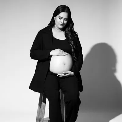 A quiet, contemplative moment captured in a black and white studio portrait. The mom-to-be is seated, gently holding her belly, creating a simple yet powerful image about the bond with her baby.