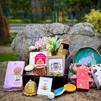 Our classic Diwali hamper, beautifully displayed outdoors. This gift box is filled with coffee cookies, jars of nuts, traditional Indian sweets, decorative diyas, and a personalized photo frame, making it a complete festive package.