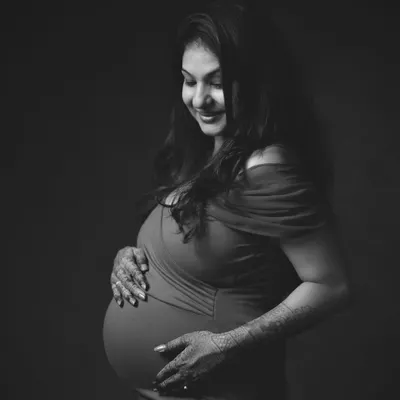 This elegant black and white studio portrait offers a different style of maternity photography. By removing color, we emphasize the beautiful curves of the baby bump and the mother's serene expression, creating a timeless and artistic image.