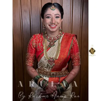 A radiant bride in her muhurtham attire. This red blouse features dense, all-over zardosi embroidery, paired with a classic off-white Kanjivaram saree for a timeless South Indian bridal look.