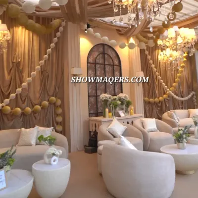 An elegant lounge area designed for a daytime event. The decor features plush ivory sofas, draped fabrics, and balloon garlands, creating a comfortable and luxurious space for guests to relax.
