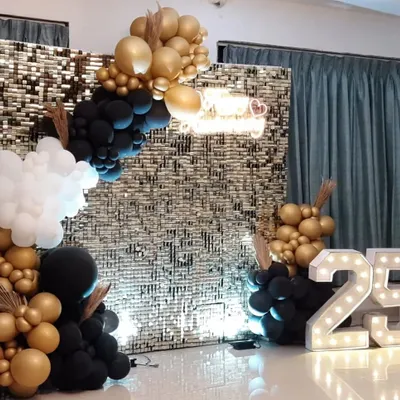 We create stunning backdrops for milestone events, like this 25th-anniversary party. The setup includes a gold shimmer wall, a 'Happy Anniversary' neon sign, and an elegant balloon arch in gold, black, and white.