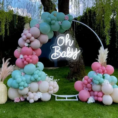A beautiful outdoor baby shower setup with a circular frame. The decor features a balloon arrangement in pastel pink, teal, and white, and an 'Oh Baby' neon sign, creating a perfect photo opportunity.