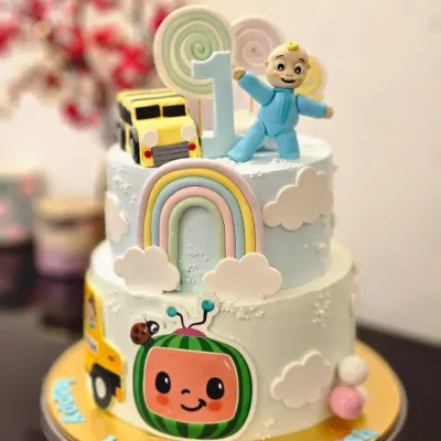 A cheerful two-tier Cocomelon cake for a first birthday. This cake features JJ, the iconic watermelon, and the yellow school bus, all brought to life with colorful details.