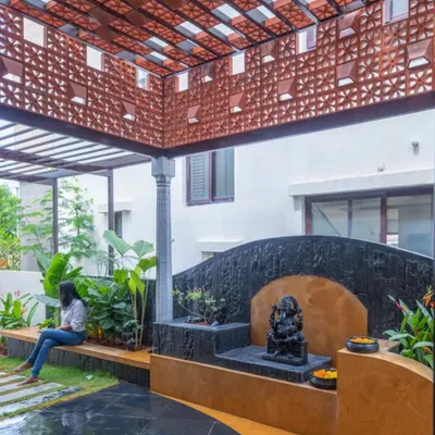 This sacred space is designed for contemplation. A Ganesha statue sits on a dark stone pedestal, surrounded by planters and set against a terracotta jaali screen that provides privacy while allowing light and air to pass through.