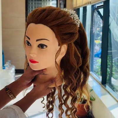 A mannequin head is used to demonstrate a romantic half-up, half-down hairstyle. This features soft curls and a twisted crown, adorned with delicate white flowers, perfect for a special occasion.