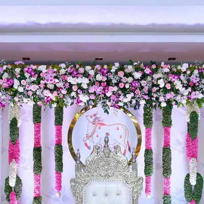 A close-up of the backdrop from a traditional Seemantham. This shows the detail of the fresh flower valance, the hanging garlands, and the custom-printed motif of the holy cow, Kamadhenu, which is significant in these ceremonies.
