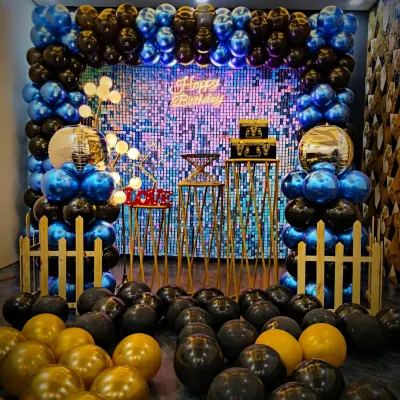 A bold and stylish birthday setup featuring a full frame of blue, black, and gold chrome balloons. The design is enhanced by a shimmering backdrop, a "Happy Birthday" neon sign, and gold disco ball accents for that extra sparkle.