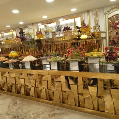 A full view of a luxurious buffet line with a geometric, reflective gold counter. This setup for an indoor event features a wide array of salads, main courses, and fruit displays, showcasing variety and opulence.