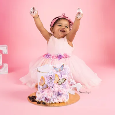 Pure joy and celebration as a little girl, dressed in a lovely pink frock, throws her hands up in delight during her butterfly-themed first birthday cakesmash.