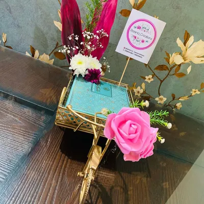 We love finding creative ways to present your return gifts. Here, a gift box is presented in a charming, gold-finished miniature cycle rickshaw, decorated with a pink rose for a whimsical touch.
