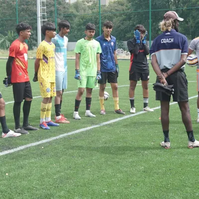 A coach observes and instructs a line of young goalkeepers before a drill. Attention to detail and correct positioning are fundamental principles we instill from a young age.