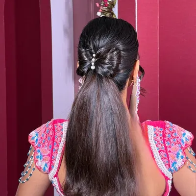 The ultimate "Barbie" ponytail. This style is sleek, high-shine, and features a beautifully crafted bow made from hair, accented with pearls for a touch of elegance.
