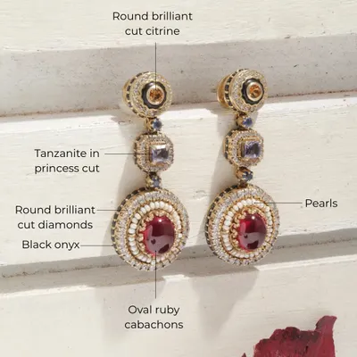 A detailed view of the iconic Crimson Royal earrings. This piece is a treasure trove of gems, featuring oval ruby cabochons, princess cut tanzanite, round brilliant citrine, pearls, and black onyx accents.