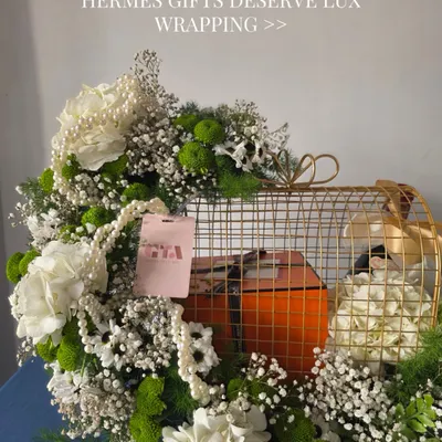 A luxury gift deserves a grand entrance. Here, I've placed a signature orange Hermès box inside a golden cage, surrounded by an explosion of white and green florals to create an unforgettable unboxing experience.