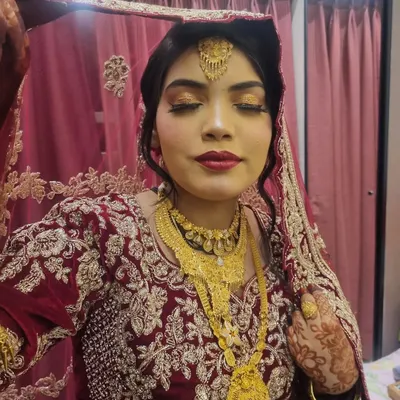 A beautiful Muslim bridal look. The makeup features golden eyes and a deep red lip, perfectly complementing her gold jewelry and embroidered outfit.