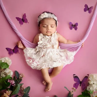 Like a little fairy sleeping in a garden. This setup features a soft fabric hammock, surrounded by flowers and butterflies, creating a beautiful and whimsical portrait for a baby girl.