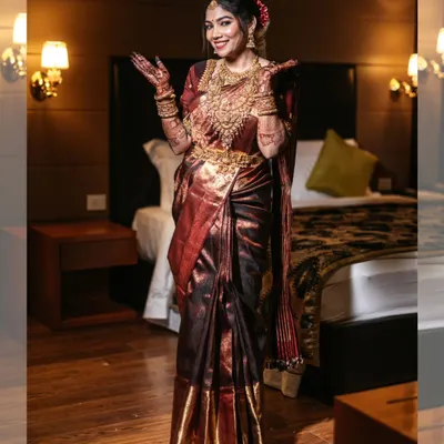 A joyful bridal portrait, capturing the bride's excitement and her stunning, shimmering saree in a warmly lit room.