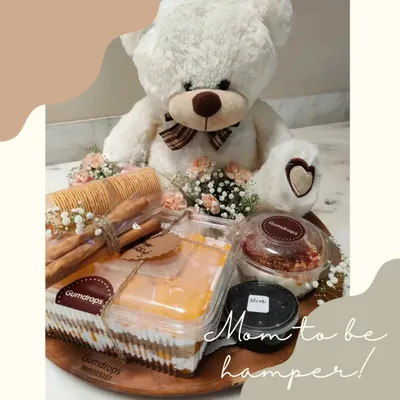 Our special 'Mom-to-be' hamper, featuring a cute teddy bear alongside delicious treats like Mango Pudding, Paprika Garlic Cream Cheese, crackers, and olives.