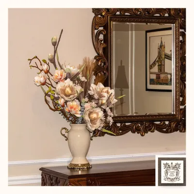 This rich, ornate mirror serves as a beautiful backdrop for a classic floral arrangement. Its detailed frame adds a vintage and elegant atmosphere, reflecting the beauty of the room.