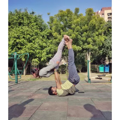 A classic Acro Yoga pose called "Bird" being performed in a park. This partner exercise is fantastic for building core strength for the base and balance for the flyer.
