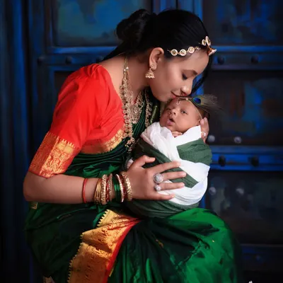 A timeless portrait capturing the tender bond between a mother and her newborn. Dressed in a beautiful traditional saree, she holds her baby close, creating a classic and emotional image against a deep blue, artistic backdrop.