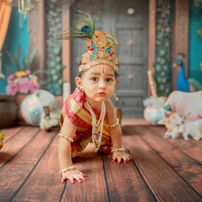A crawling 'Little Krishna' on a mission. This dynamic shot captures a key baby milestone within the vibrant Janmashtami theme, complete with a peacock feather crown and traditional jewelry.
