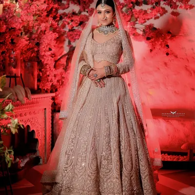 A stunning full-length portrait of a bride in a pastel-toned lehenga against a dramatic red floral wall. This shot shows how we use contrast to make the bride and her outfit the undeniable center of attention.