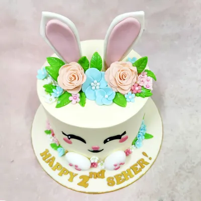 We craft pure pastel joy with this adorable bunny face cake. Perfect for a second birthday, this design features a sweet bunny face with large ears peeking out from a crown of delicate, handcrafted sugar flowers in soft peach and blue.