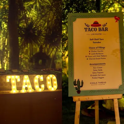 The setup for a memorable taco party. A custom menu board details the delicious fillings and accompaniments, next to our illuminated "TACO" sign, creating an inviting and festive atmosphere for your guests.