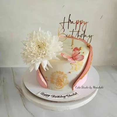 A pretty birthday cake featuring a large fresh chrysanthemum, a hand-painted butterfly, and a delicate fondant wrap. The gold stenciling adds a touch of elegance to the design.