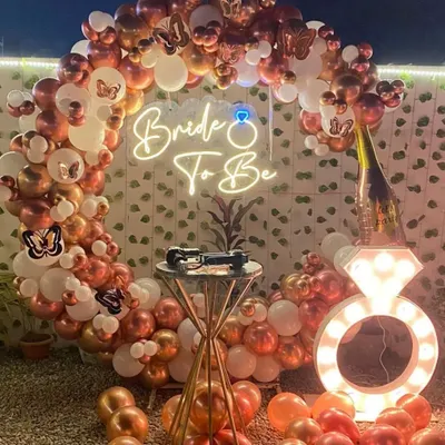 This is a very popular 'Bride to Be' party setup for an outdoor or terrace space. It features a circular balloon arch in rose gold and white, a neon sign, butterfly accents, and a large, light-up diamond ring prop for photos.