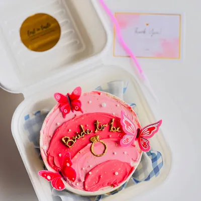 A beautiful "Bride to be" bento cake perfect for a bridal shower or bachelorette party. It features an ombre pink design, a gold ring detail, and decorative butterflies.