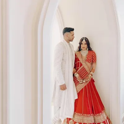 The stunning couple, Carla and Arjun, in a quiet moment. Carla's classic red Sabyasachi lehenga is beautifully contrasted by Arjun's elegant all-white sherwani, creating a timeless and romantic visual.