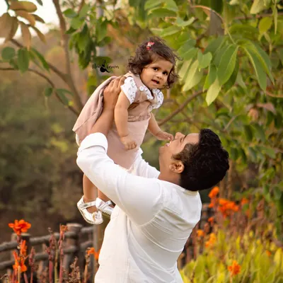 A father lifts his daughter up against a backdrop of lush greenery and flowers. Outdoor family photography sessions like this one are perfect for capturing playful, natural moments in the golden hour light.