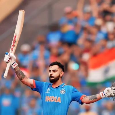 The king raises his bat. An iconic shot of Virat Kohli celebrating a milestone, with the Indian flag and cheering crowd creating a patriotic and energetic backdrop.