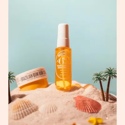 A summer-themed shot for a body mist, using sand, seashells, and miniature palm trees. This creative setup instantly communicates the product's beachy, tropical vibe.
