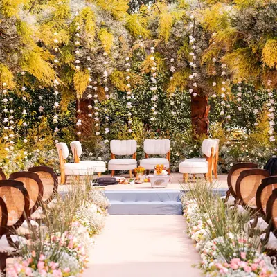 A breathtaking outdoor mandap setup for a day wedding, with lush greenery and hanging floral arrangements creating a fairytale atmosphere.