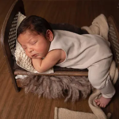 A newborn peacefully sleeping in a miniature wooden bed. I use props like these to highlight just how tiny and precious they are in their first days.