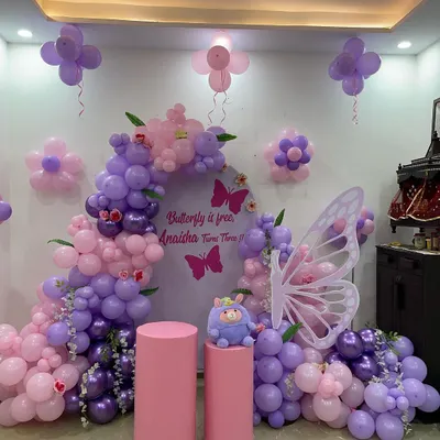 A beautiful butterfly-themed party in shades of purple and pink. This setup features a balloon arch around a custom backdrop, large butterfly wings for photos, and flower-shaped balloon clusters on the wall.