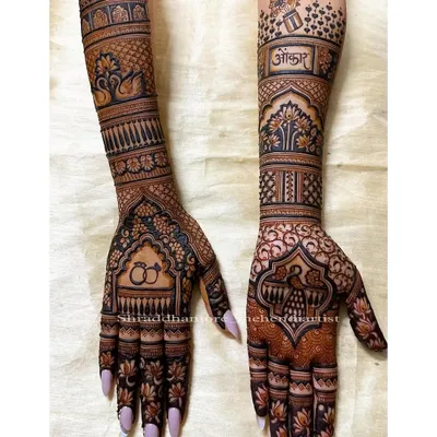 This full-arm bridal mehendi was created for Ankita, featuring her partner's name 'Omkar' on one arm and engagement rings on the other. The design combines traditional elements like swans and peacocks with personal touches.