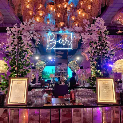 A glimpse of our elegant bar setup at the Ritz, where sophisticated design meets exceptional service. The glowing neon sign and floral arch create an inviting focal point for any reception.