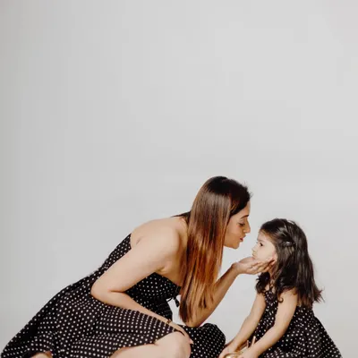 A tender moment between a mother and her daughter during their twinning photoshoot. Dressed in matching polka-dot dresses, the mother gently holds her daughter's face, creating a timeless and loving portrait.