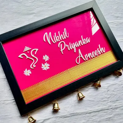 A beautiful Khun nameplate in a vibrant pink, customized in English with a Ganesha icon for blessings. The little bells at the bottom add a lovely traditional sound and look.
