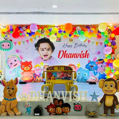 A bright and cheerful Cocomelon party stage, featuring a large personalized backdrop with the birthday boy's photo and all the main characters.